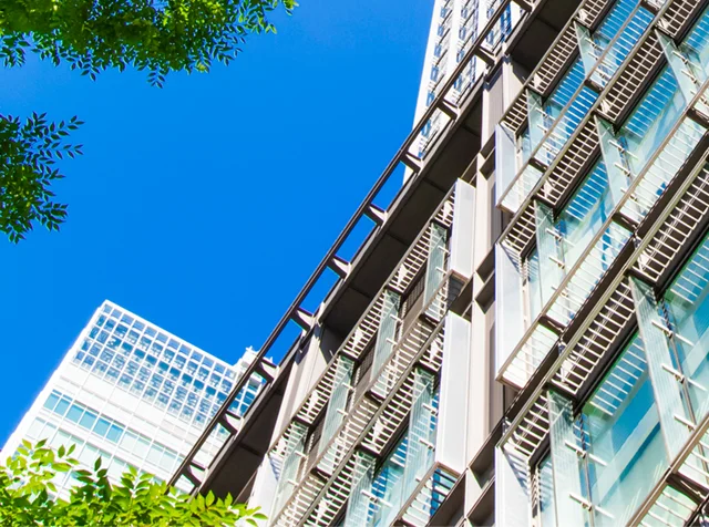 高層ビルのガラス窓に映る青空と緑の葉